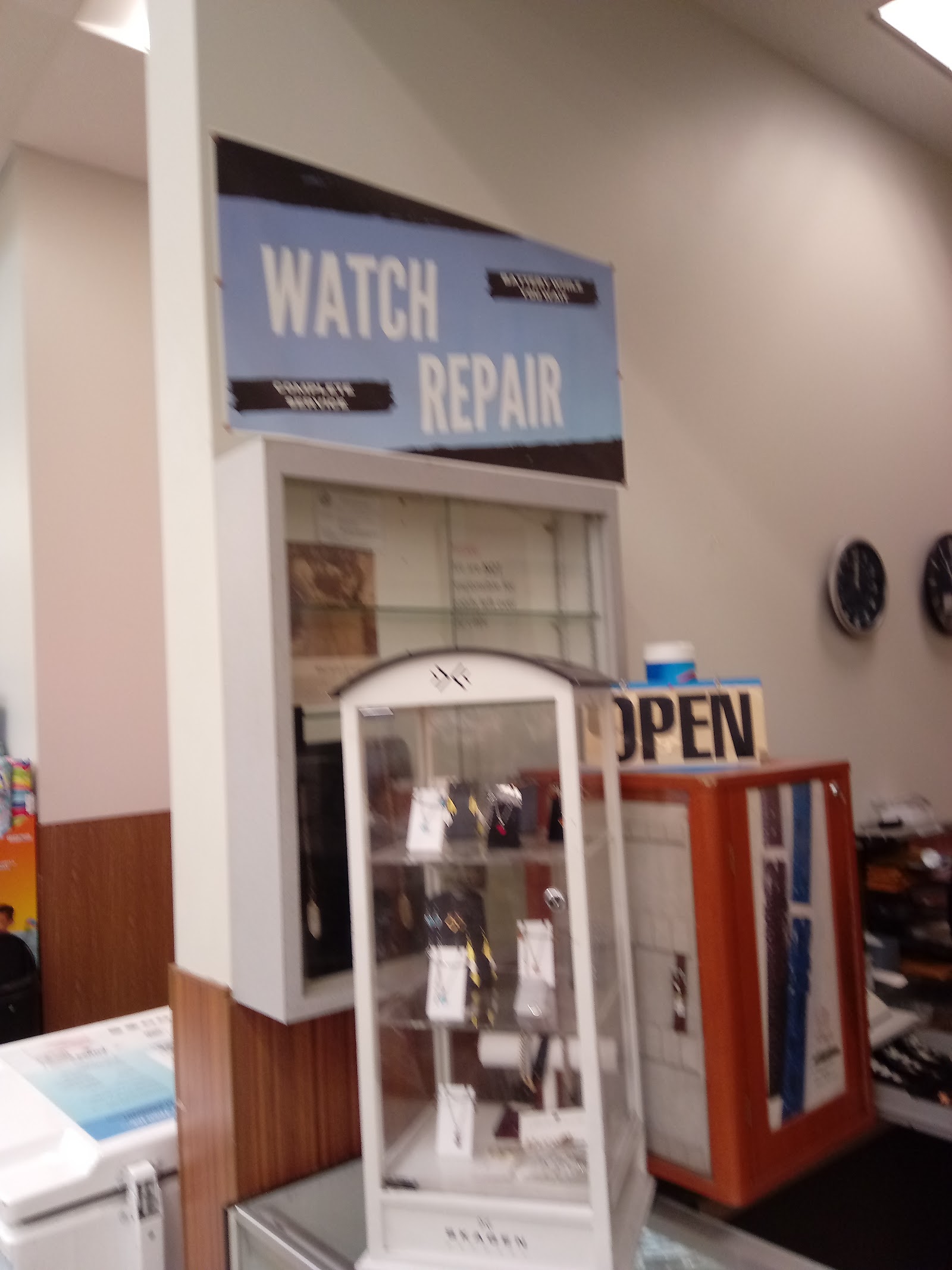 Interior of M & S Watch Gallery showing the WATCH REPAIR sign and a Skagen jewelry display case, with a vintage OPEN sign on the counter.